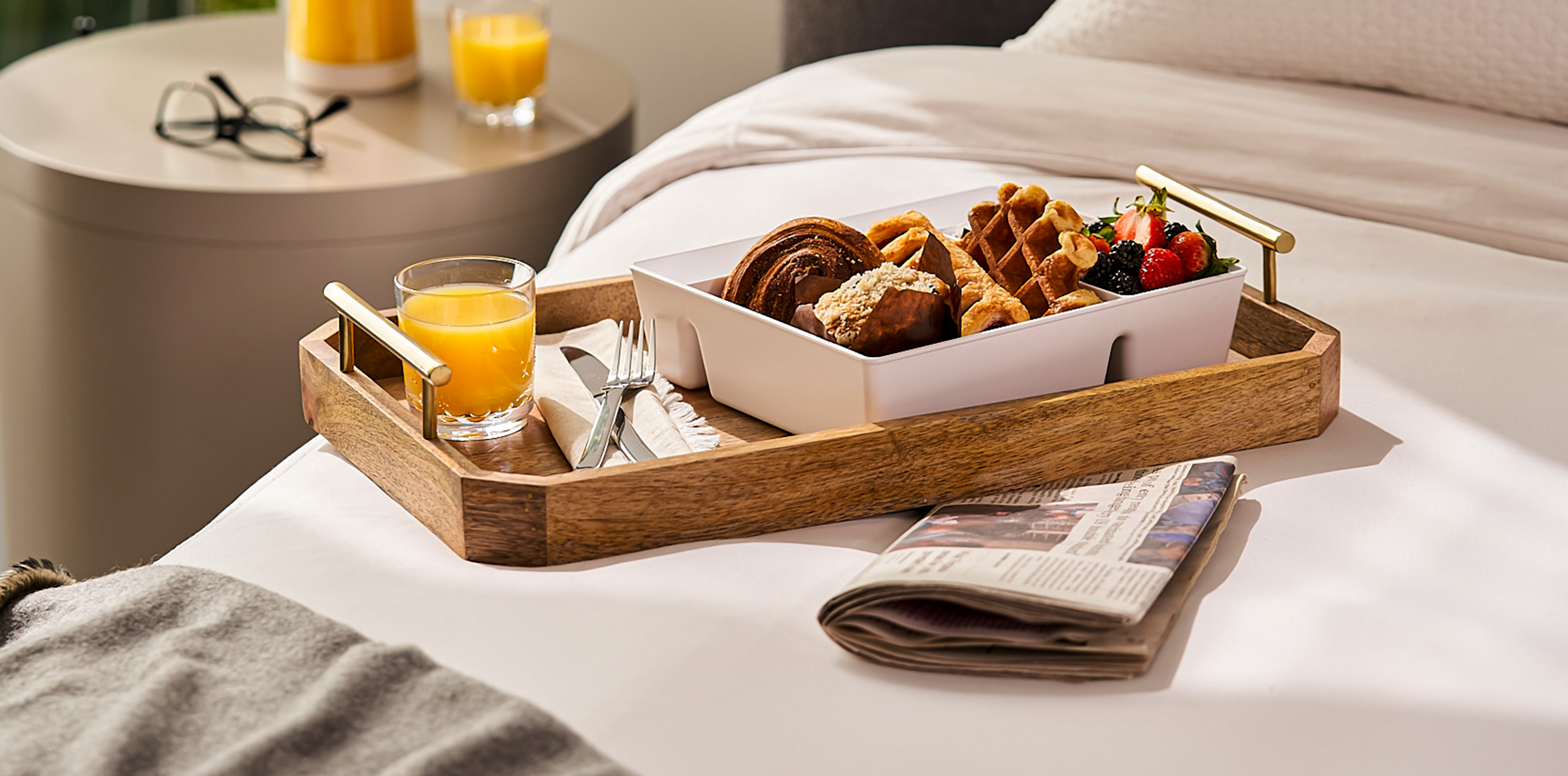 A tray with orange juice and a bento box of baked goods, waffles and fruit. 