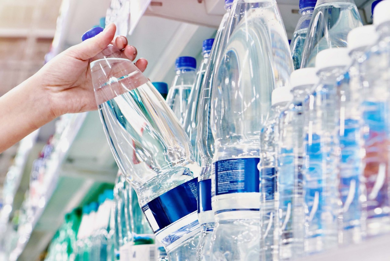 A hand grabbing a clear plastic water bottle from a grocery shelf. 