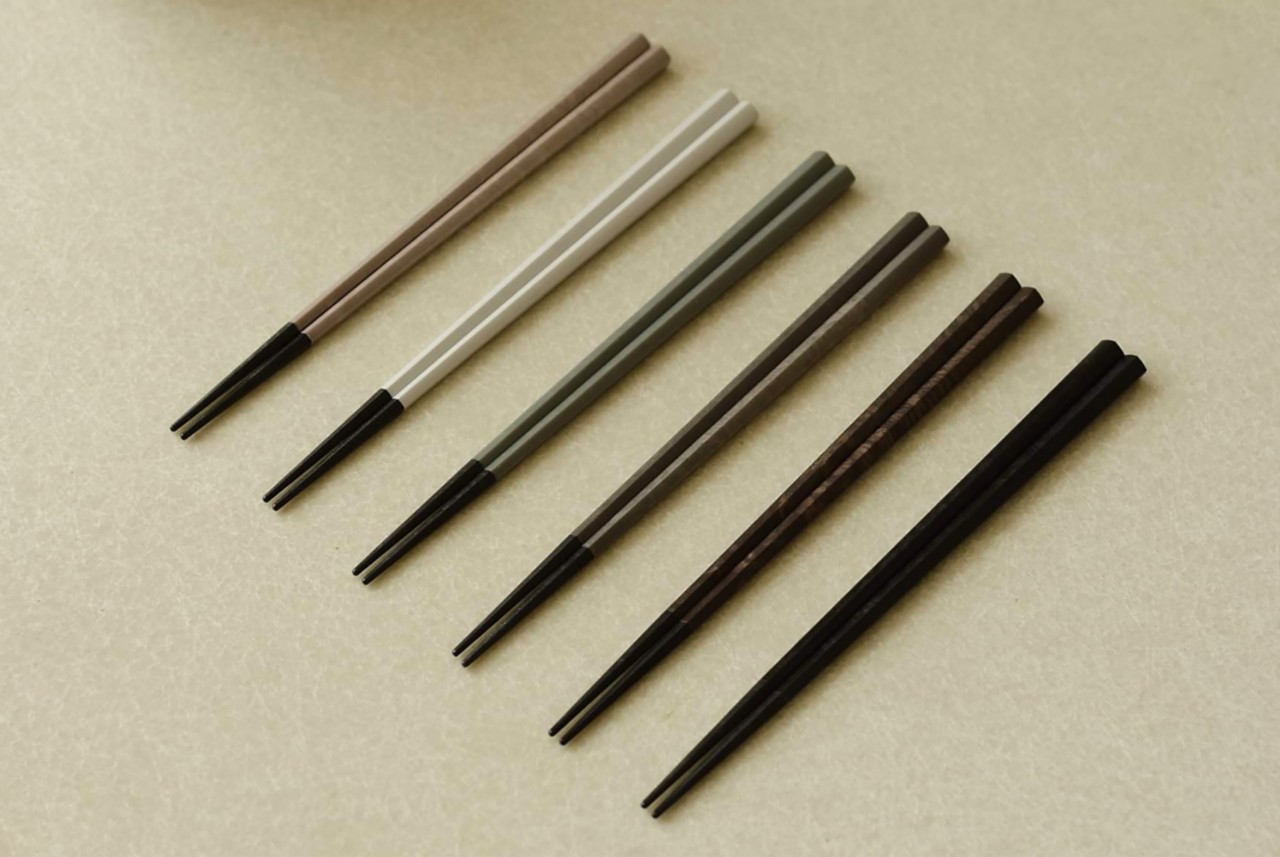 Six sets of earth-tone-colored chopsticks on a tablecloth. 