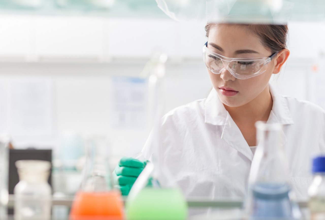 Una científica con gafas de seguridad, una bata de laboratorio y guantes en el laboratorio 
